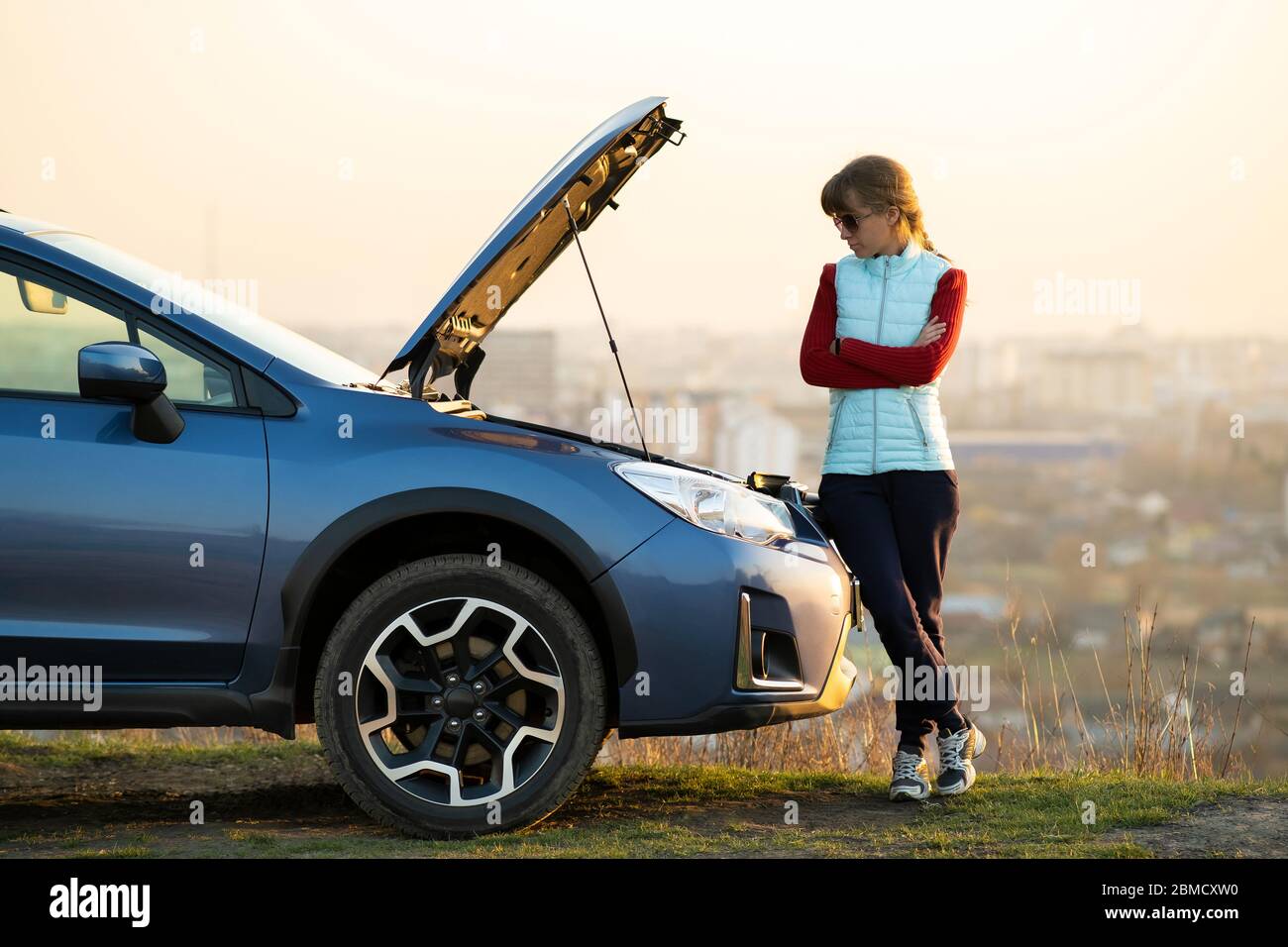 Young woman standing near broken down car with popped up hood having ...