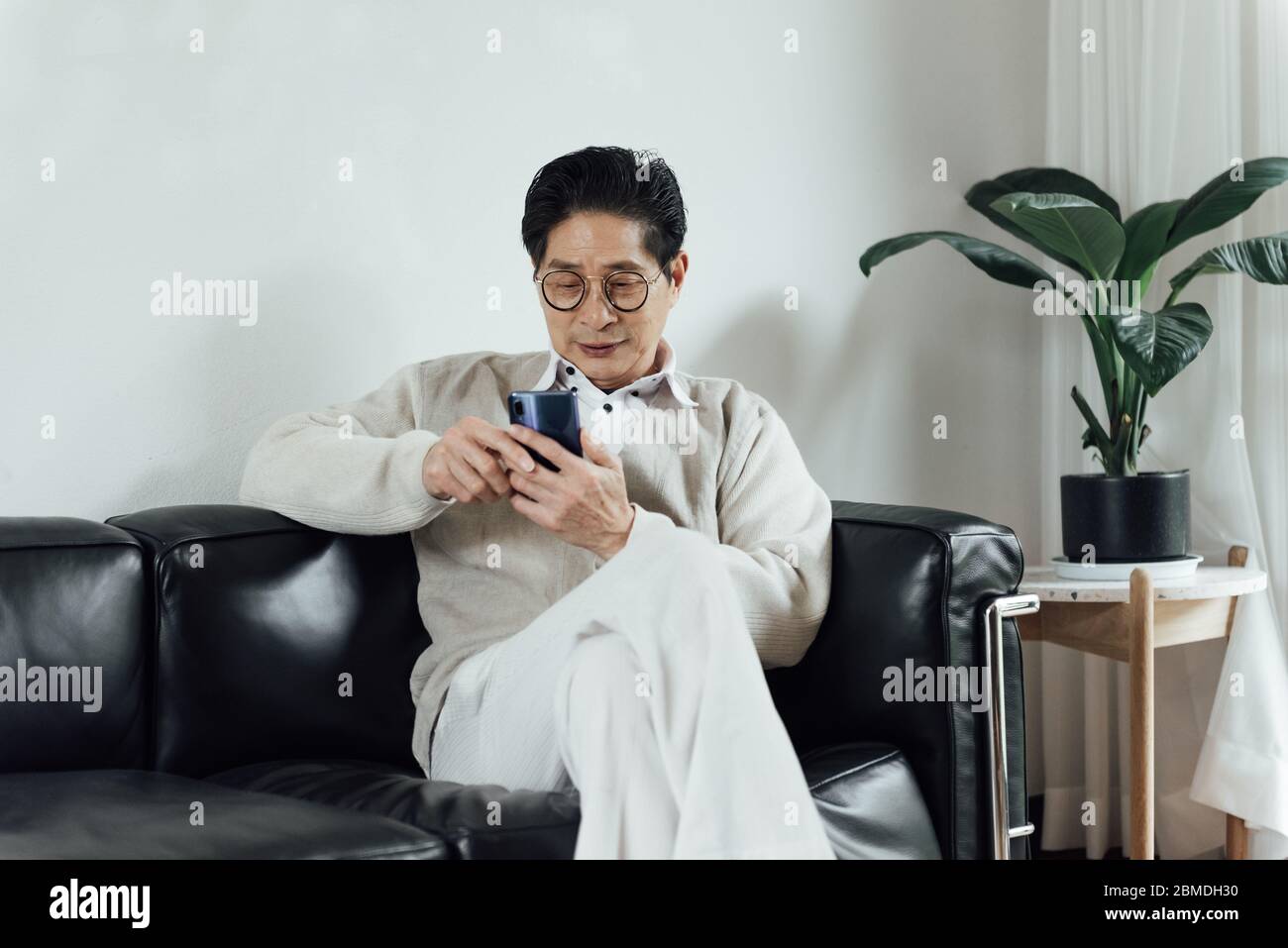 An Asian elderly man using mobile phone in the living room Stock Photo