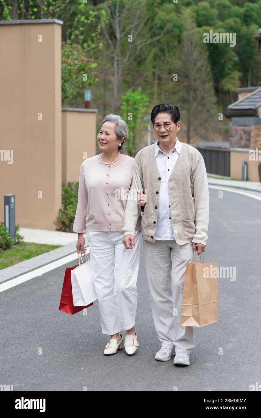 An elderly Asian couple holding shopping bags in the community Stock Photo