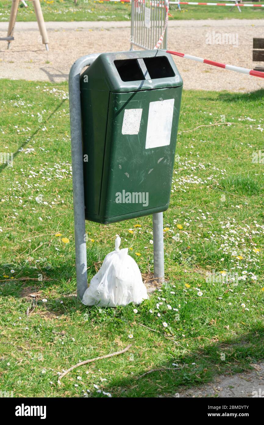 An empty public trash can with a plastic waste bag dumped underneath Stock Photo