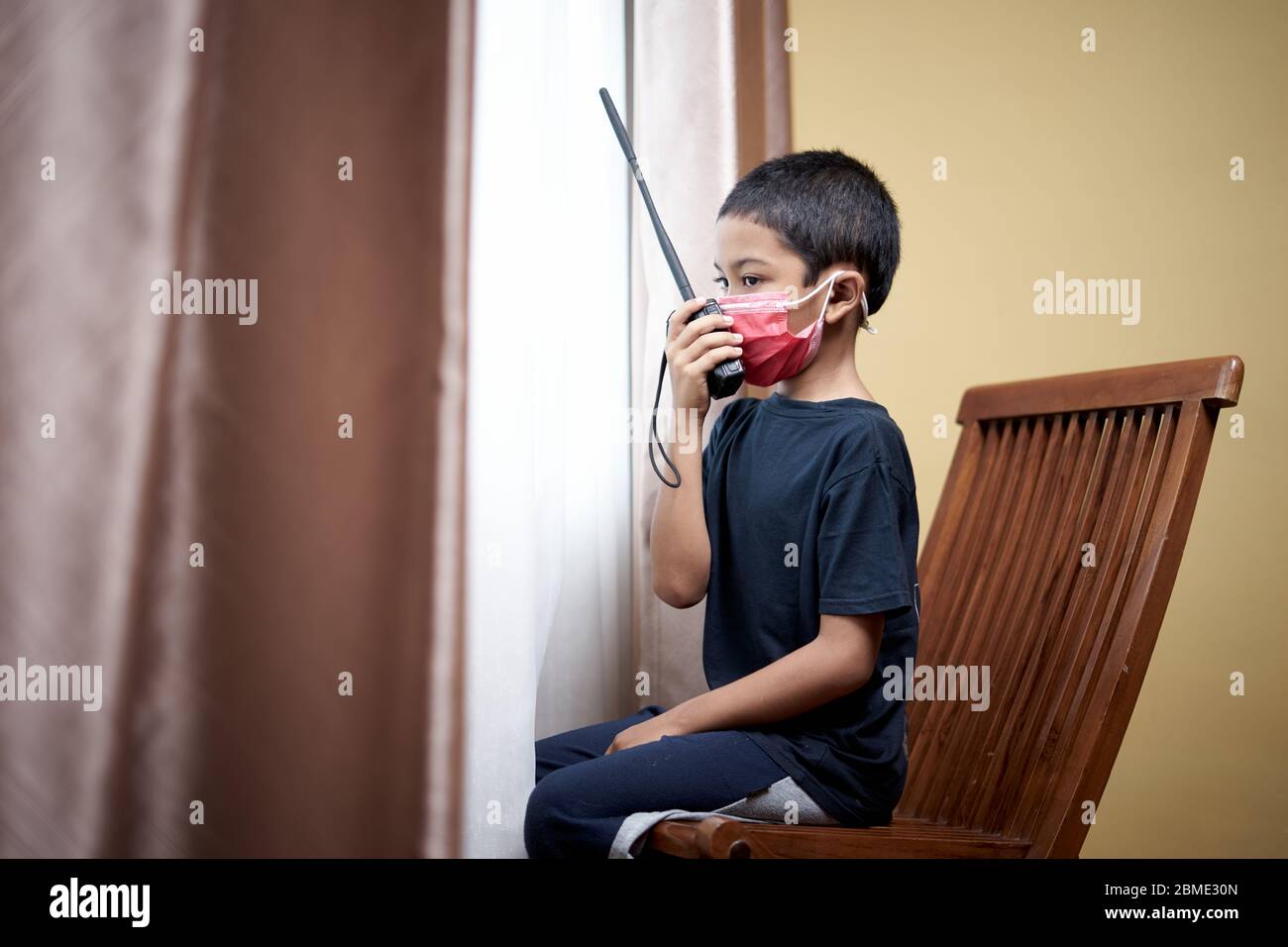 Sad little Boy communicate using walkie talkie and looking through window at home quarantine Stock Photo