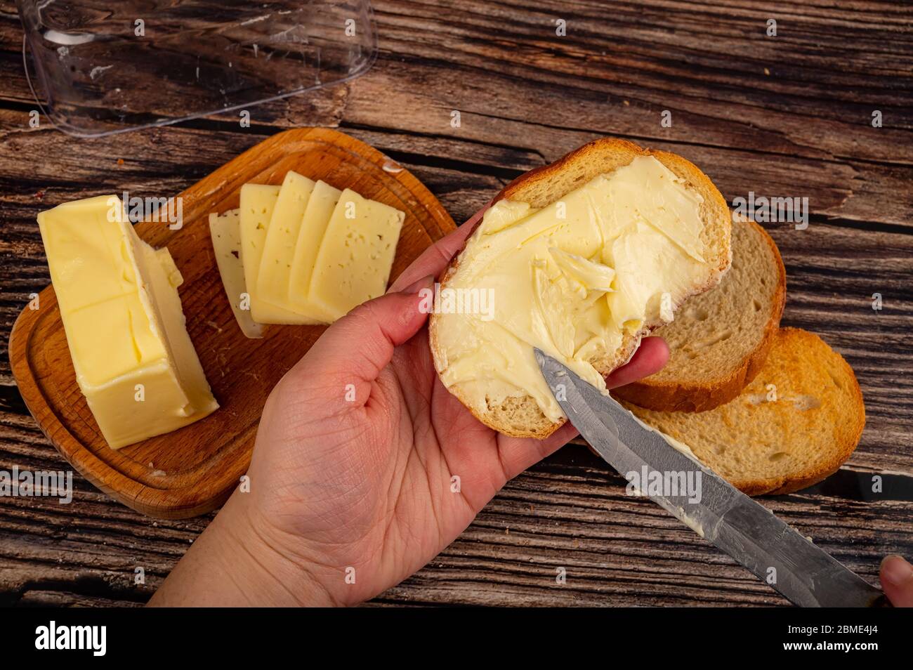 Someone spreads a little butter with a knife on fresh wheat toast, a piece of butter in a wooden