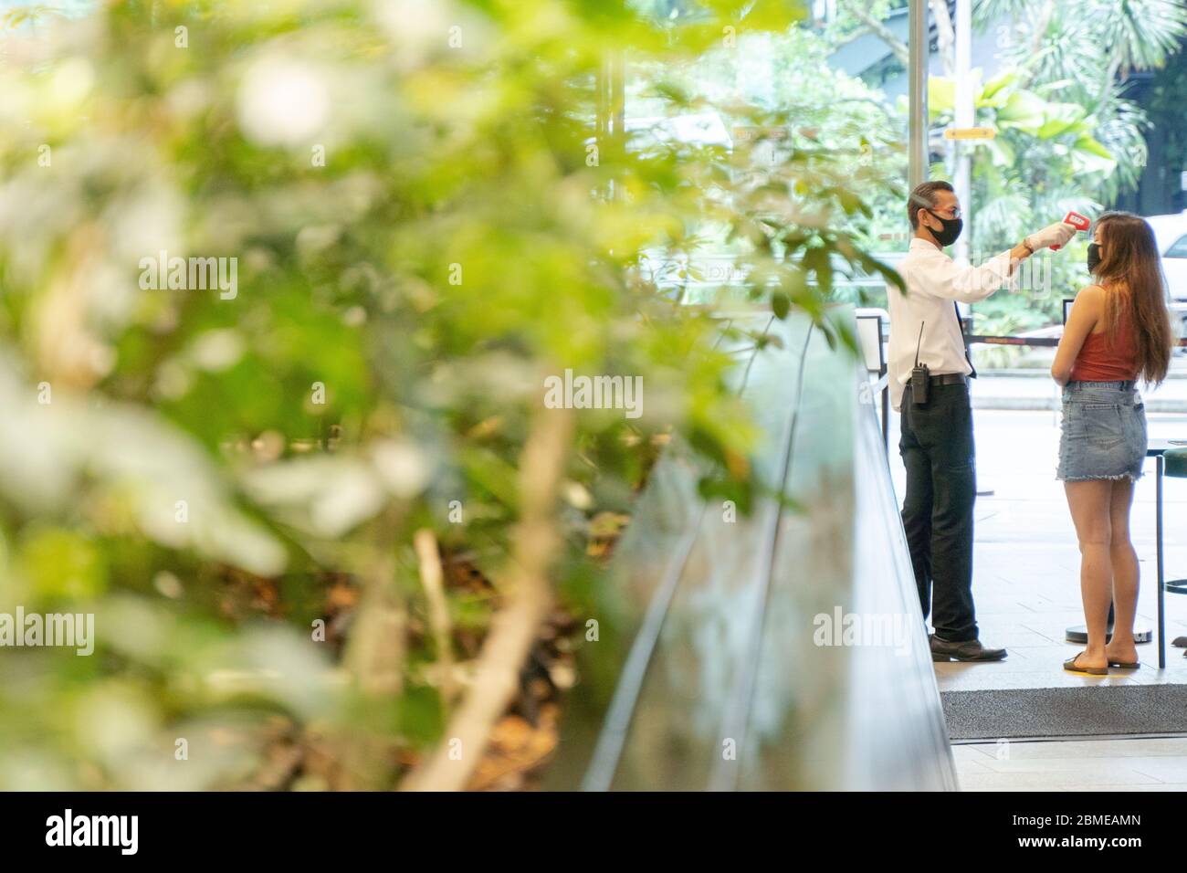Security guard taking temperature of individual entering shopping mall Stock Photo