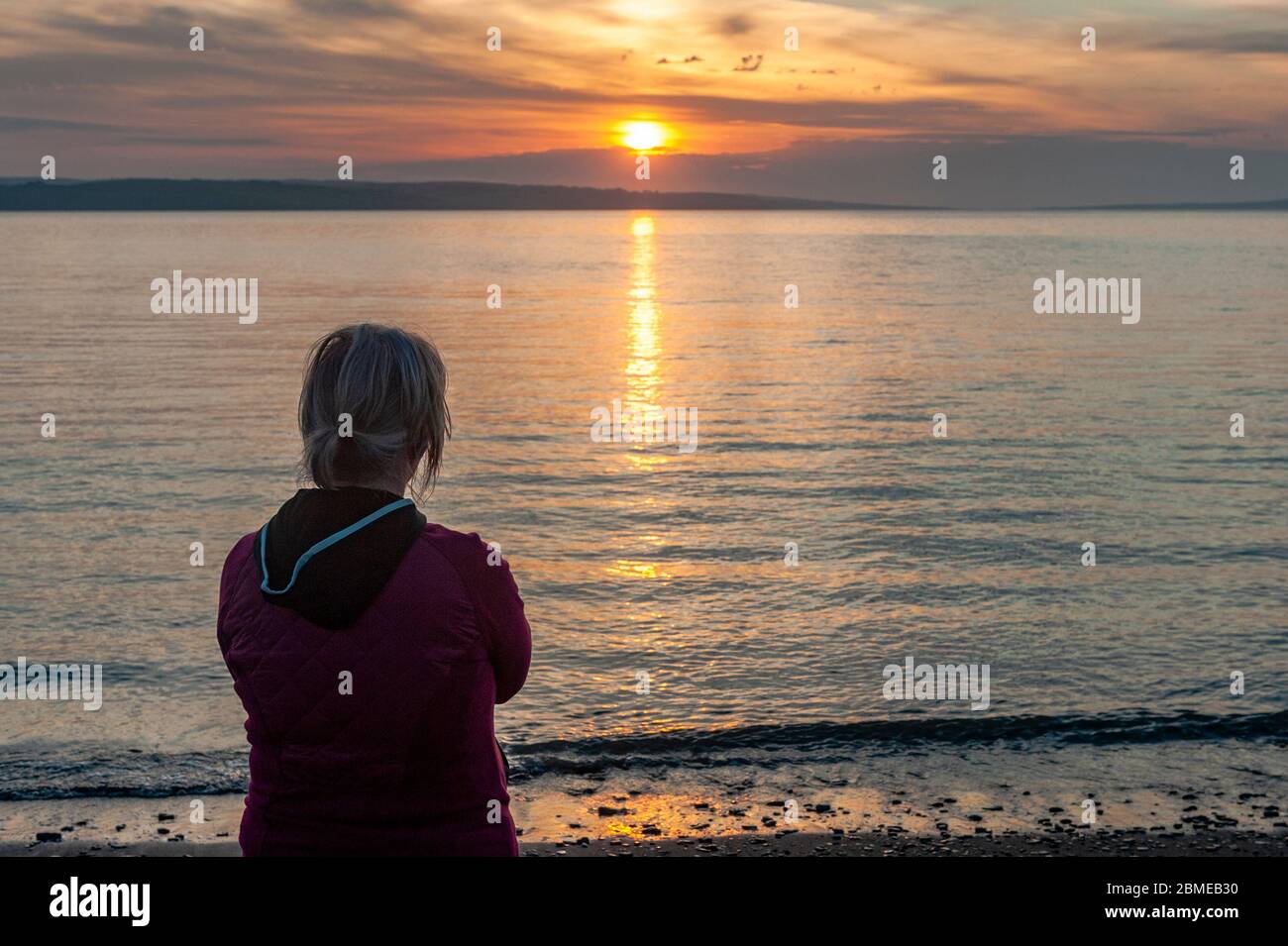 Courtmacsherry, West Cork, Ireland. 9th May, 2020. Due to the Covid-19 Lockdown, Pieta House had to cancel its Darkness into Light walk this year. However, Pieta House urged people to view the sunrise to raise money for the charity. A woman watches the sun rise at Broadstrand Beach. Credit: AG News/Alamy Live News Stock Photo