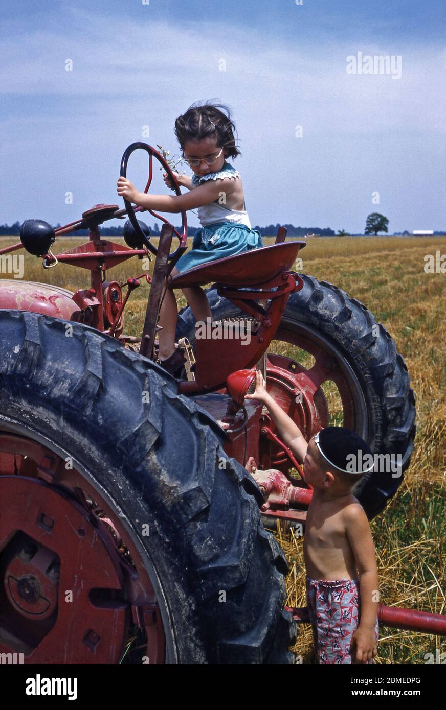 Two children playing in the sunshine on a tractor on the family farm, USA in the early 1950s. Stock Photo
