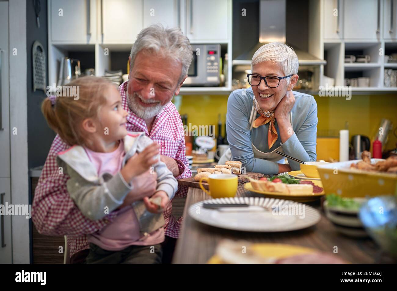 grandpa holding his granddaughter in a lap in a kitchen with grandma ...