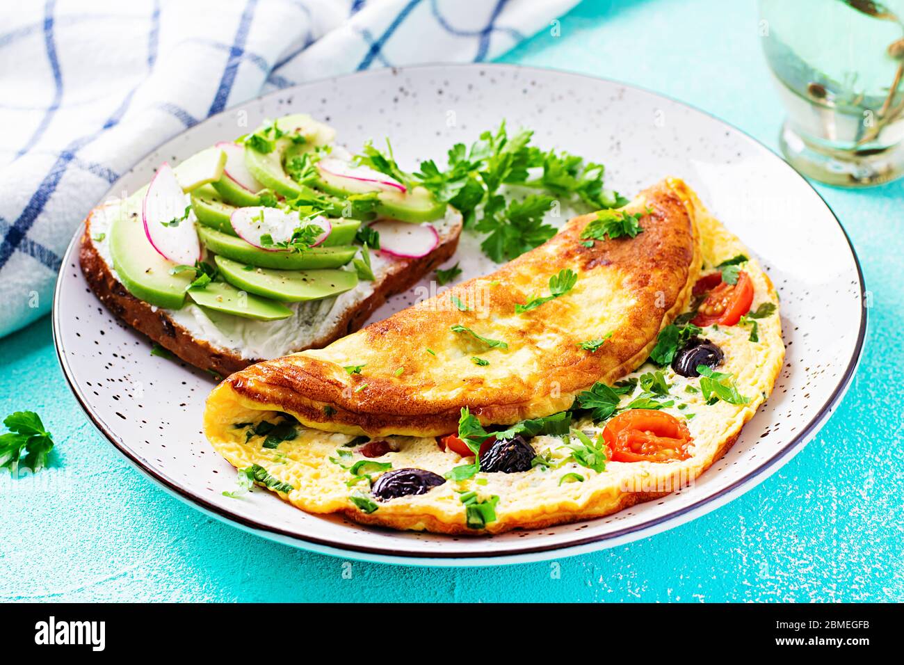 Breakfast. Omelette with tomatoes, black olives and sandwich with avocado on white plate.  Frittata - italian omelet. Stock Photo