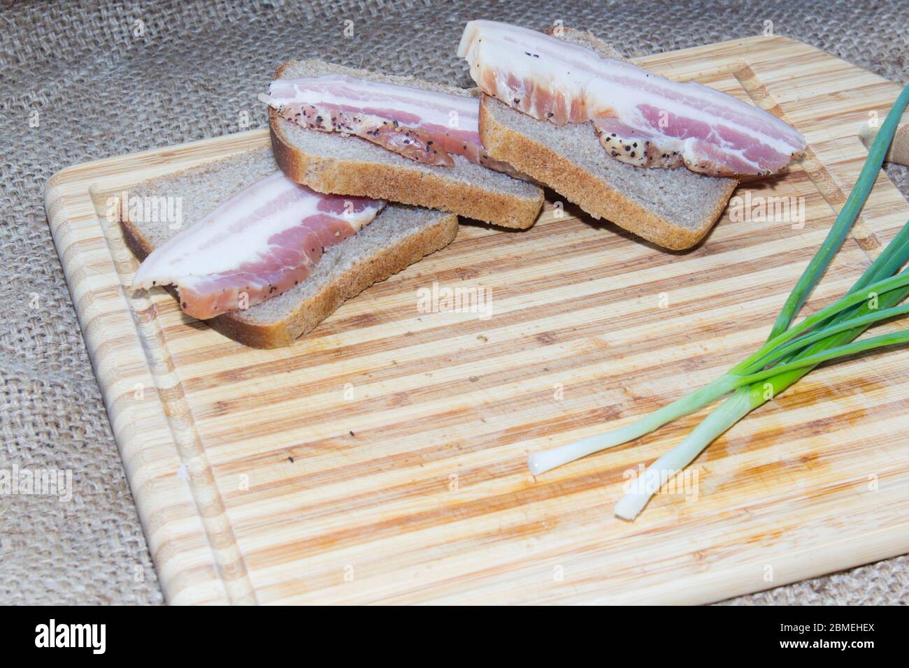 Smoked bacon, bread, green onion on a wooden cutting board Stock Photo
