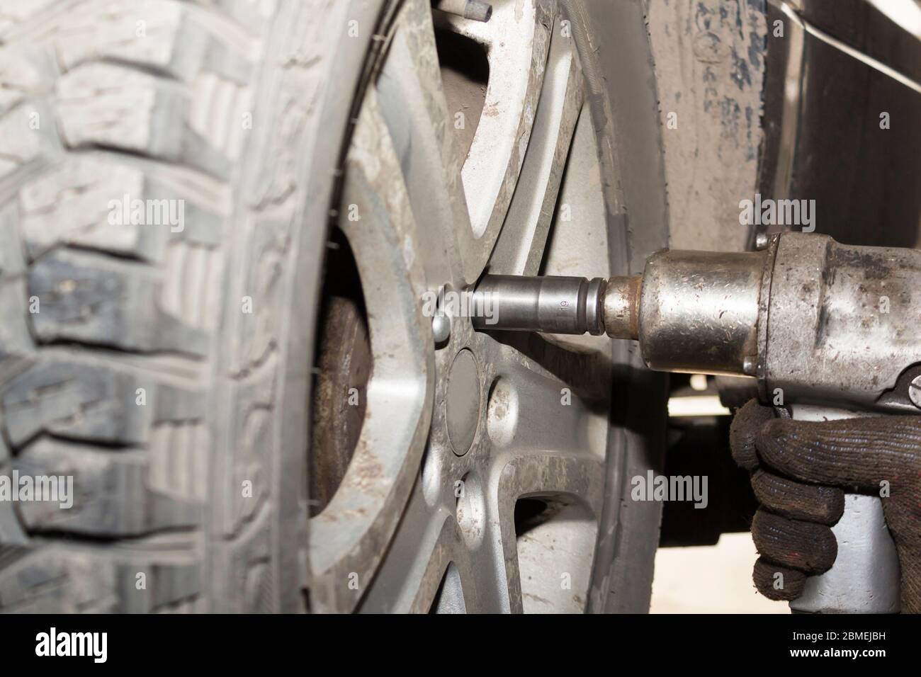 Car mechanic hands replace tires on wheels in garage. Mechanic technician worker installing car wheel at maintenance. Tire installation concept Stock Photo