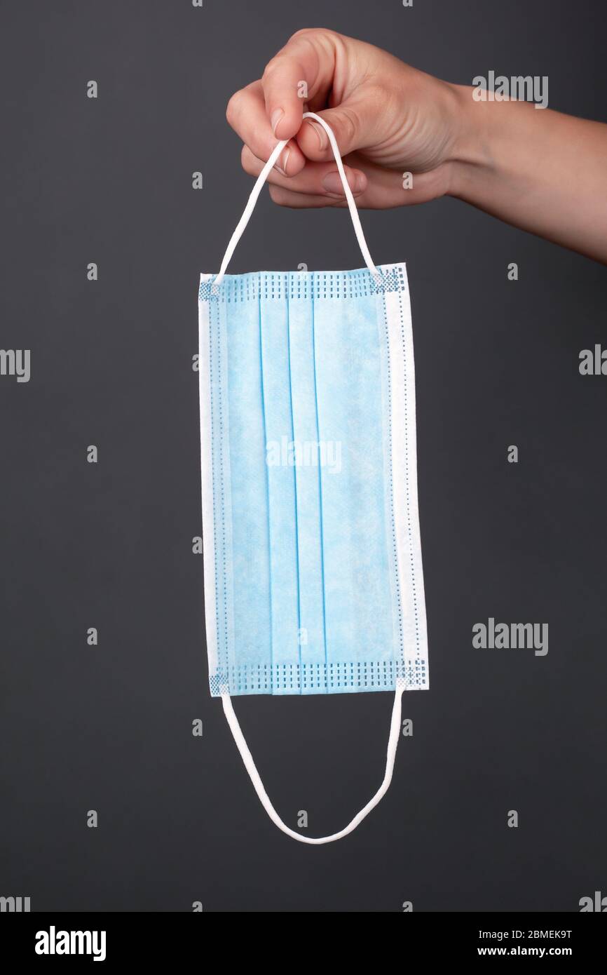 medical blue protective surgical disposable mask in hand on a dark background,  vertical, close-up.  health concept, covid-19 protection, quarantine, Stock Photo