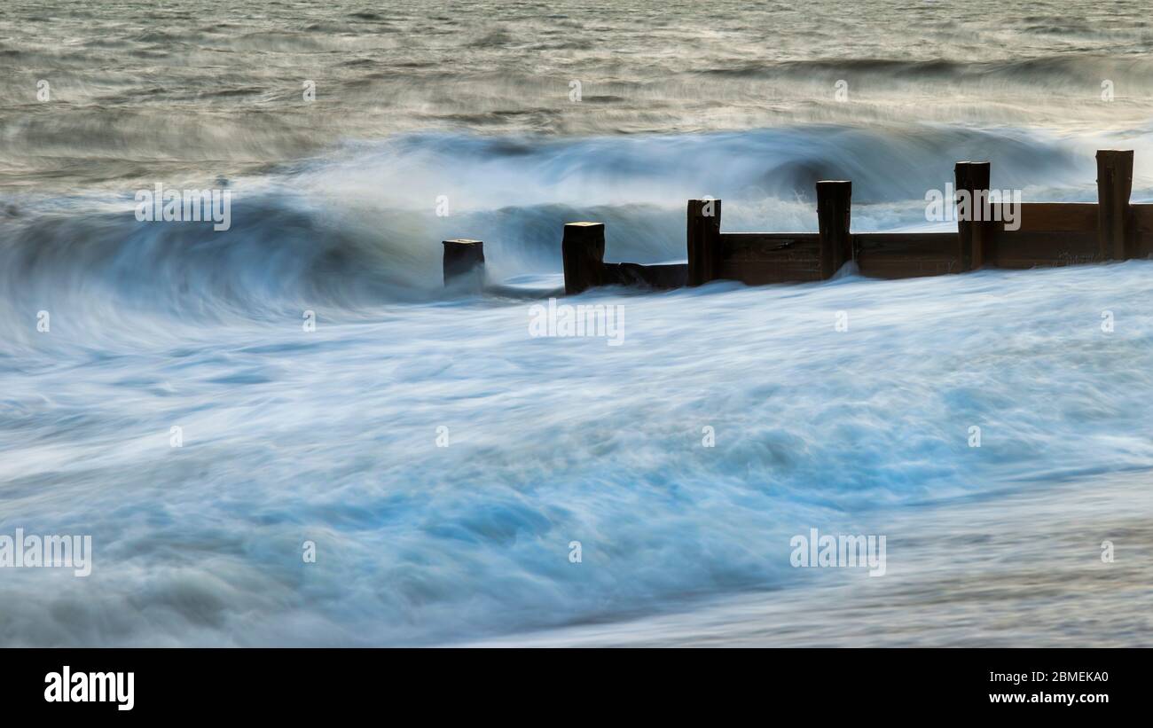 Beautiful abstract long exposure landscape image of waves crashing onto groynes on beach during sunset Stock Photo