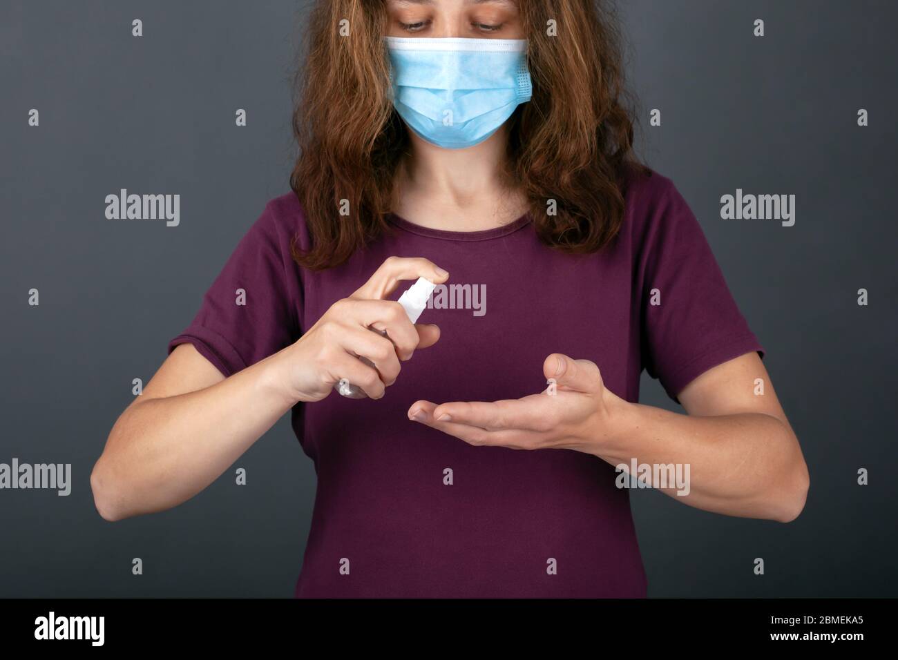 young girl in a blue medical mask holds a bottle with antibacterial spray,  disinfects hands with antiseptic. hygiene, coronavirus infection preventio Stock Photo