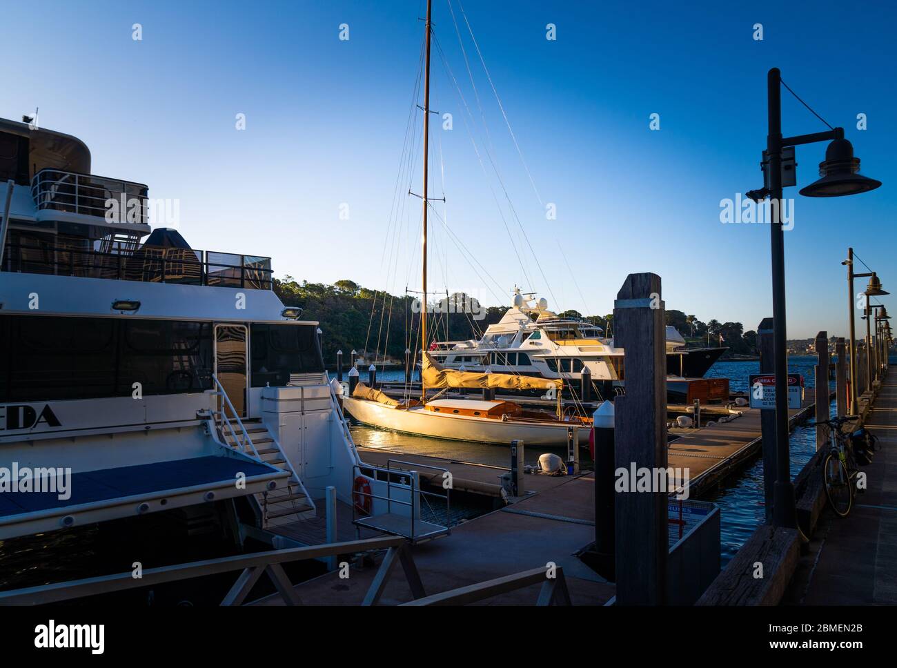 A classic old wooden yacht picked out by the sun surrounded by newer motor boats Stock Photo