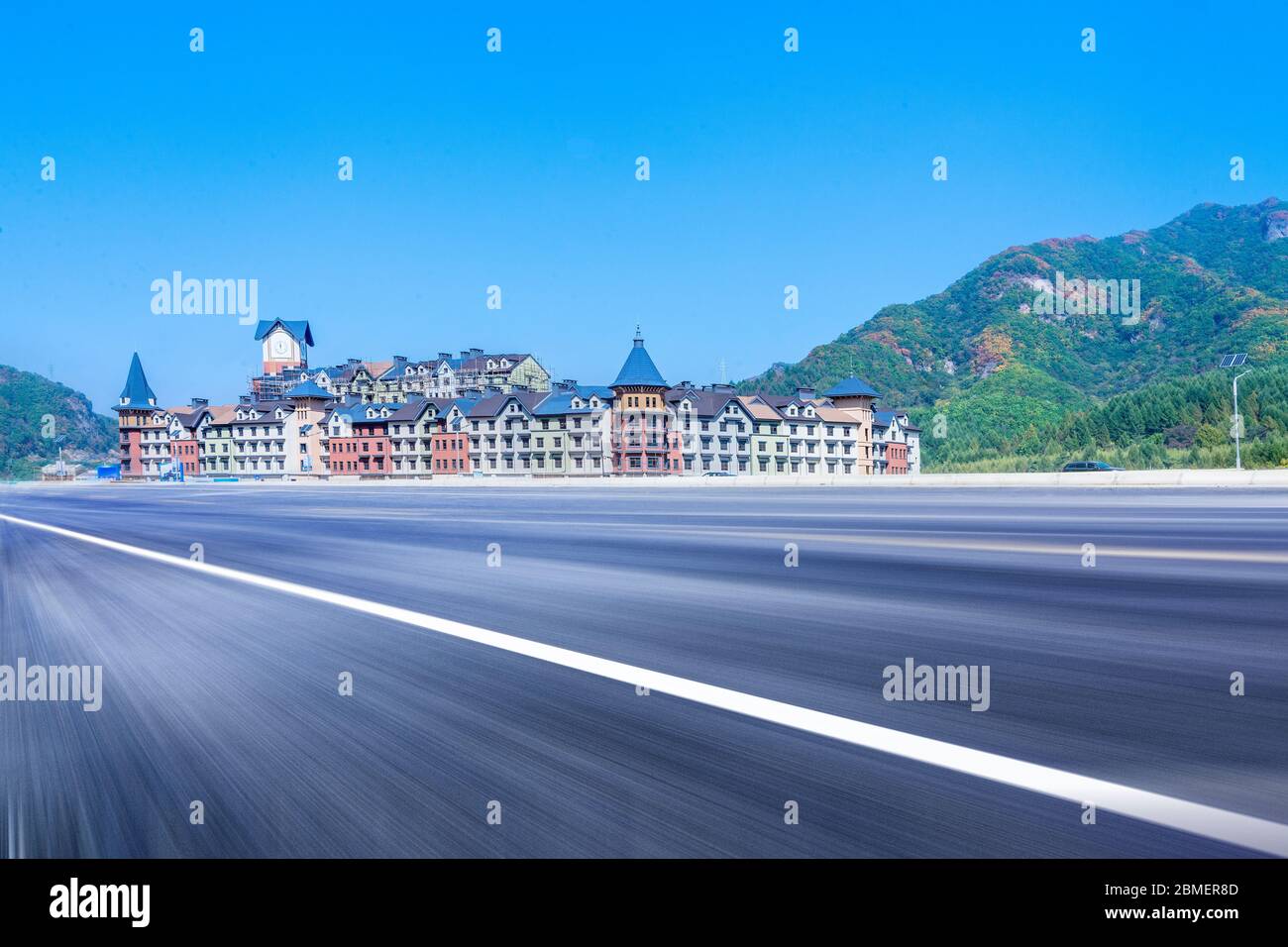 European castle building and asphalt highway under blue sky mountain. Stock Photo