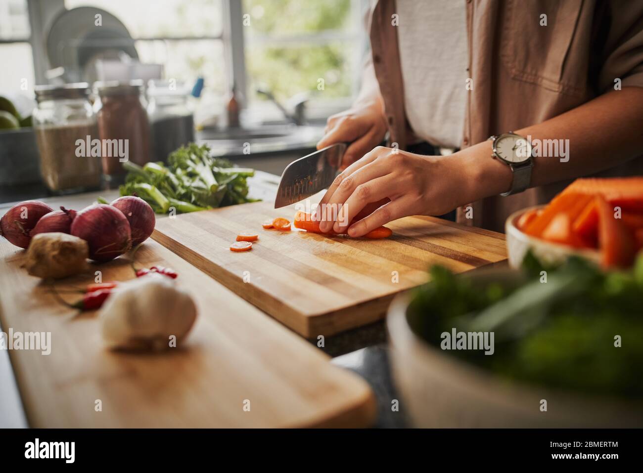 Closeup of young female hands chopping fresh orange carrot on board while in modern kitchen - healthy food to boost the immune system  Stock Photo