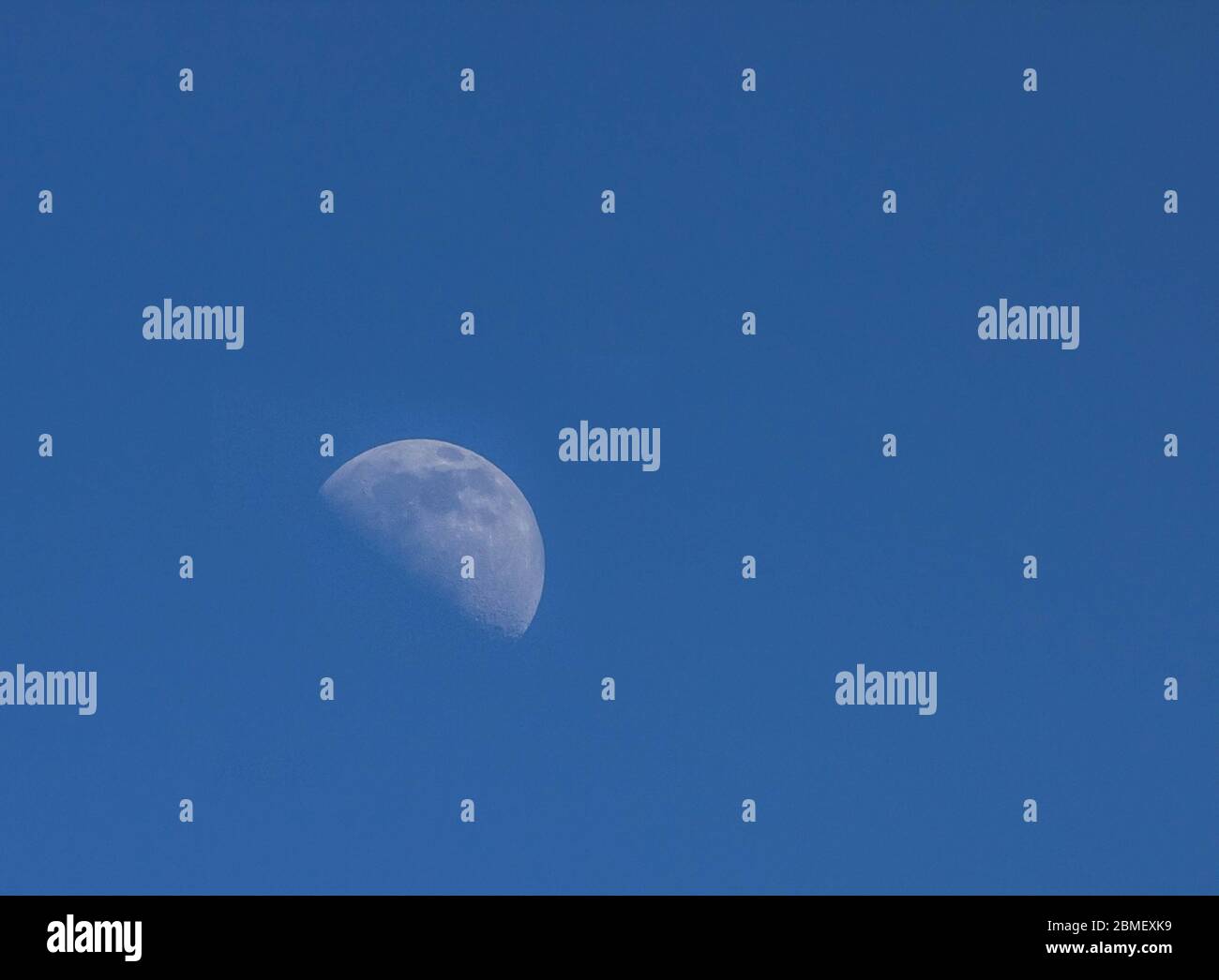 The moon, a natural satellite of the Earth a week before the full moon is filmed in the evening in a blue sky Stock Photo