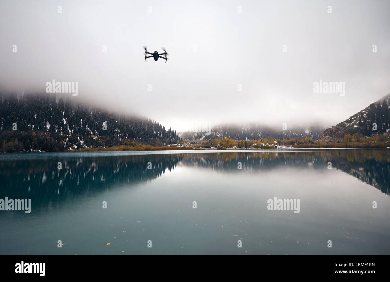 Uav drone copter flying at foggy mountain lake in autumn time Stock Photo