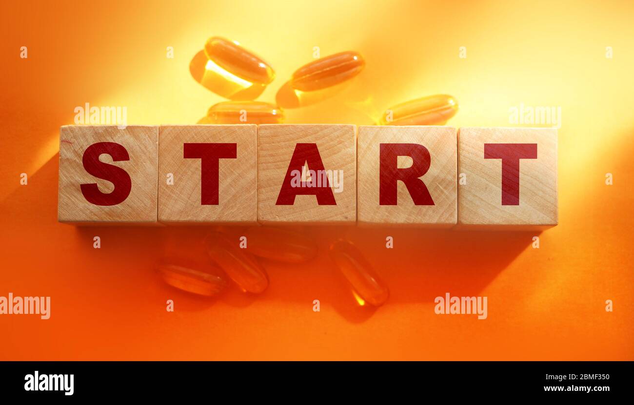 Word Start is written on wooden cubes and oil capsules on a orange background. Medical healthcare start treatment concept Stock Photo