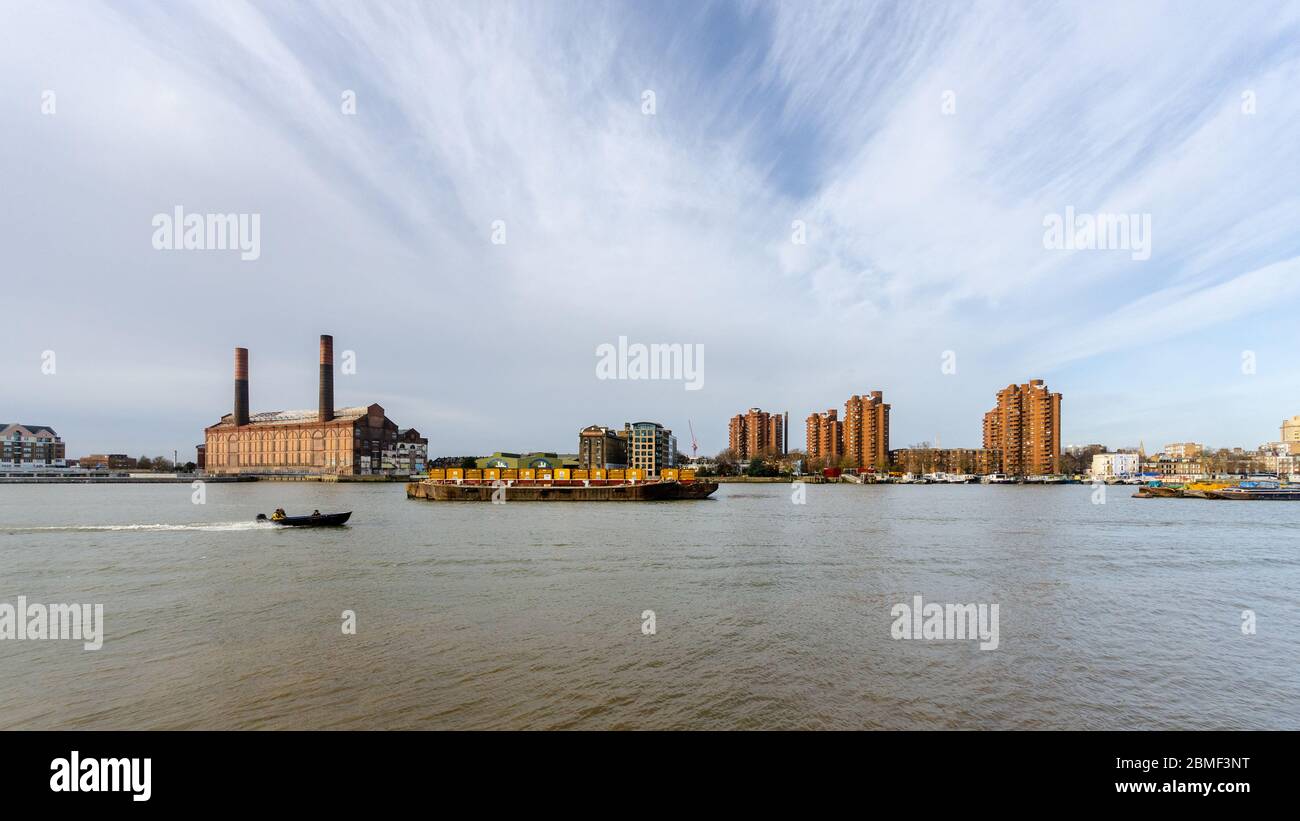 London, England, UK - December 12, 2013: A speedboat passes container barges moored beside Lots Road Power Station and the World's End Estate in the R Stock Photo