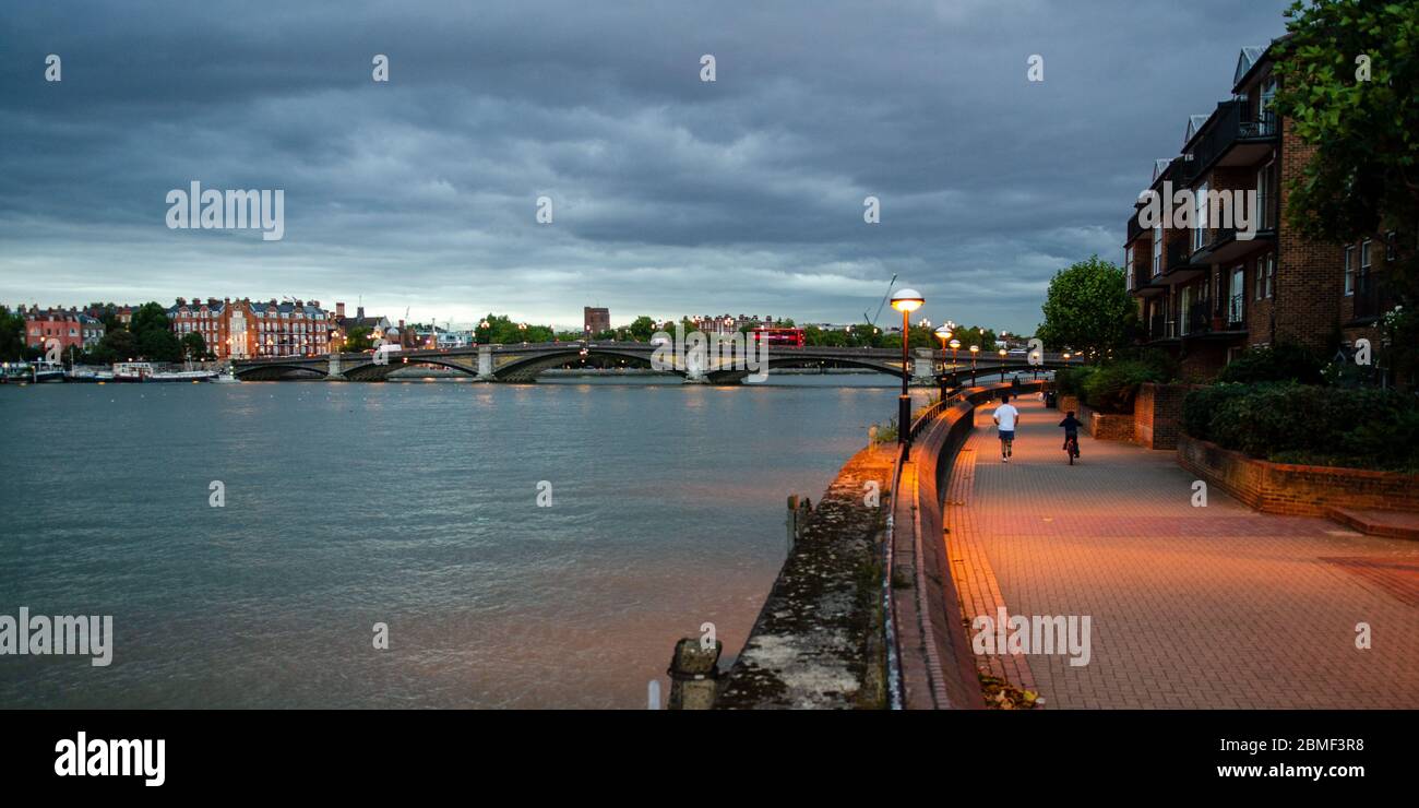 London, England, UK - October 9, 2013: Pedestrians, joggers and cyclists use the Thames Path beside Battersea Bridge, while grey clouds gather on the Stock Photo