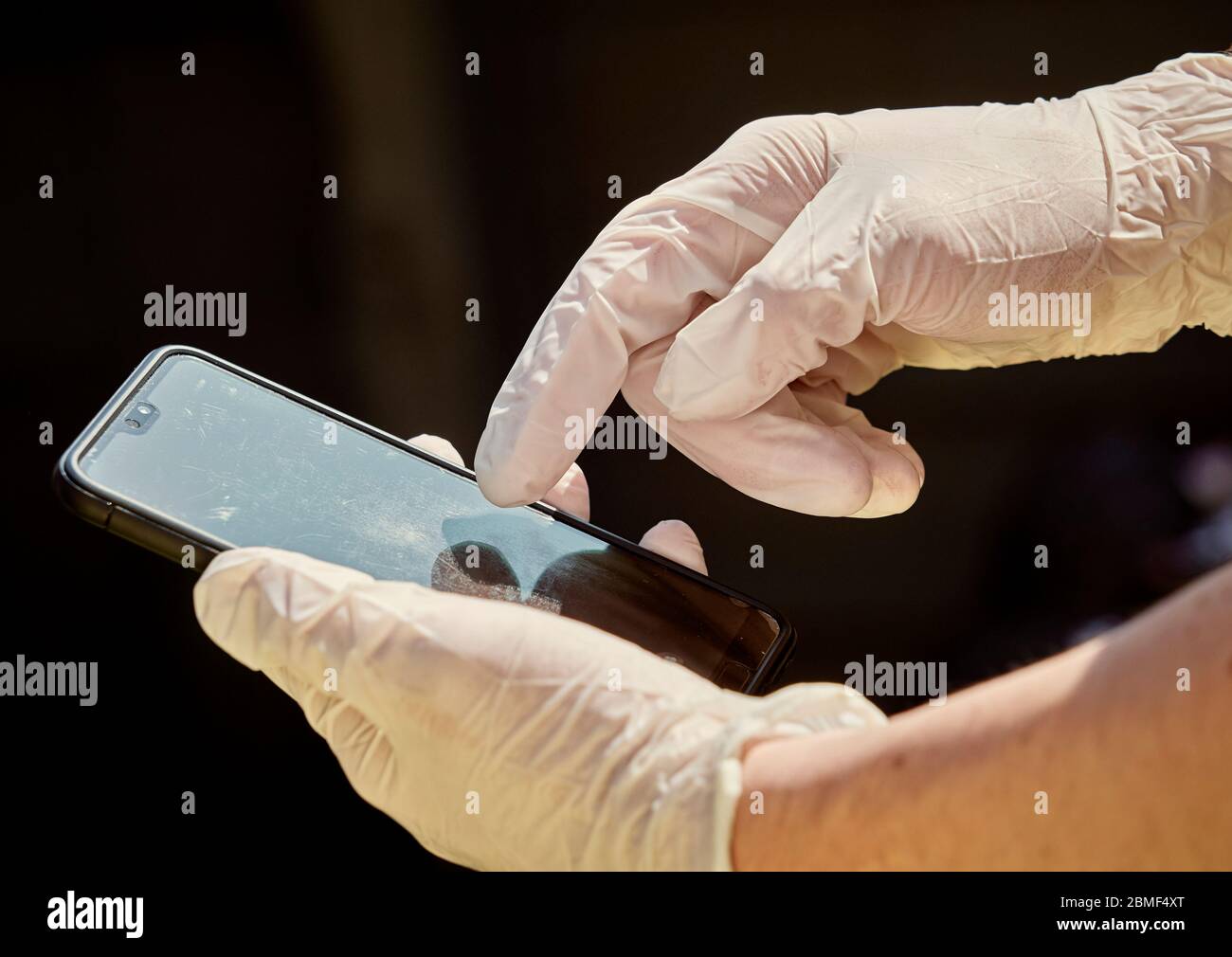 Person using a mobile phone whilst wearing medical disposable gloves aslo known as PPE Stock Photo
