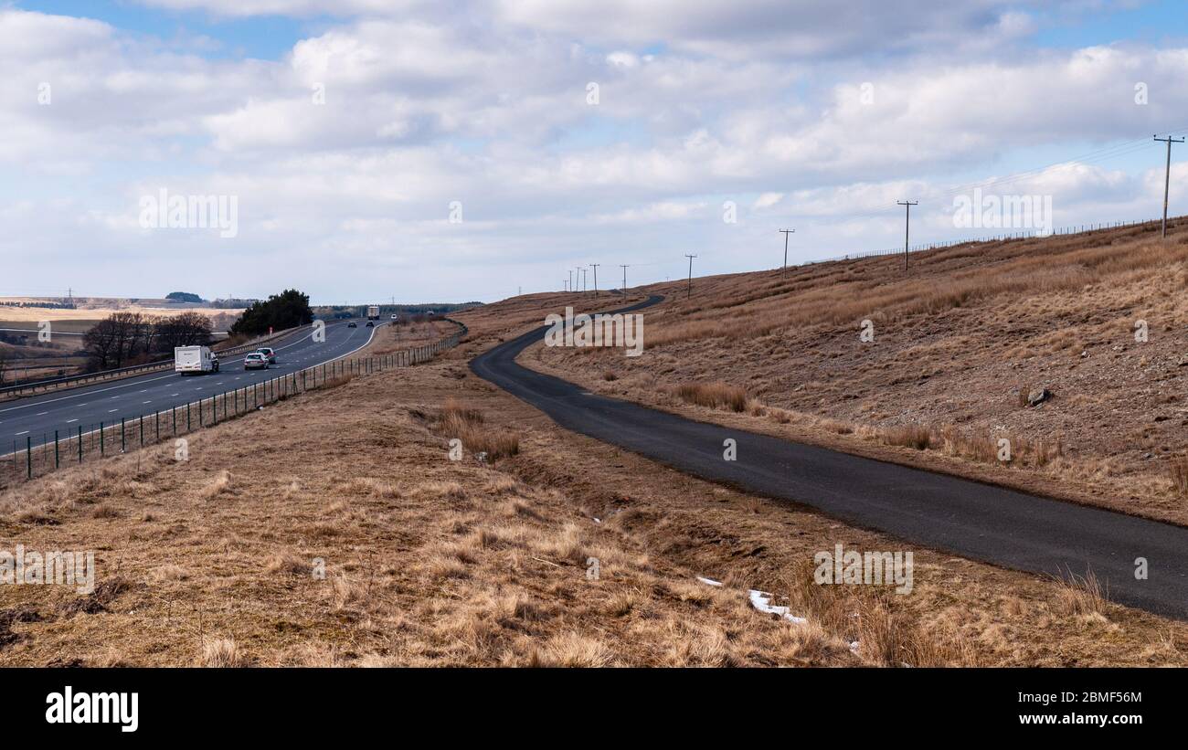 Traffic flows on the northbound M6 motorway at Orton in Cumbria, where the carriageways divide and a country lane runs between them. Stock Photo