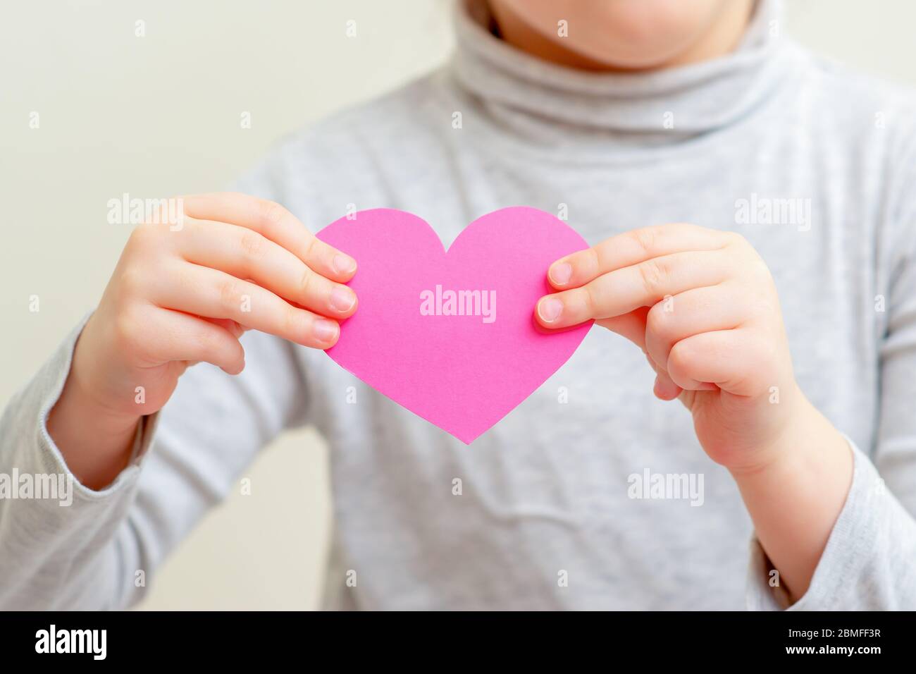 Closeup of pink paper heart in hands of child. Pink heart in child's hands. Stock Photo