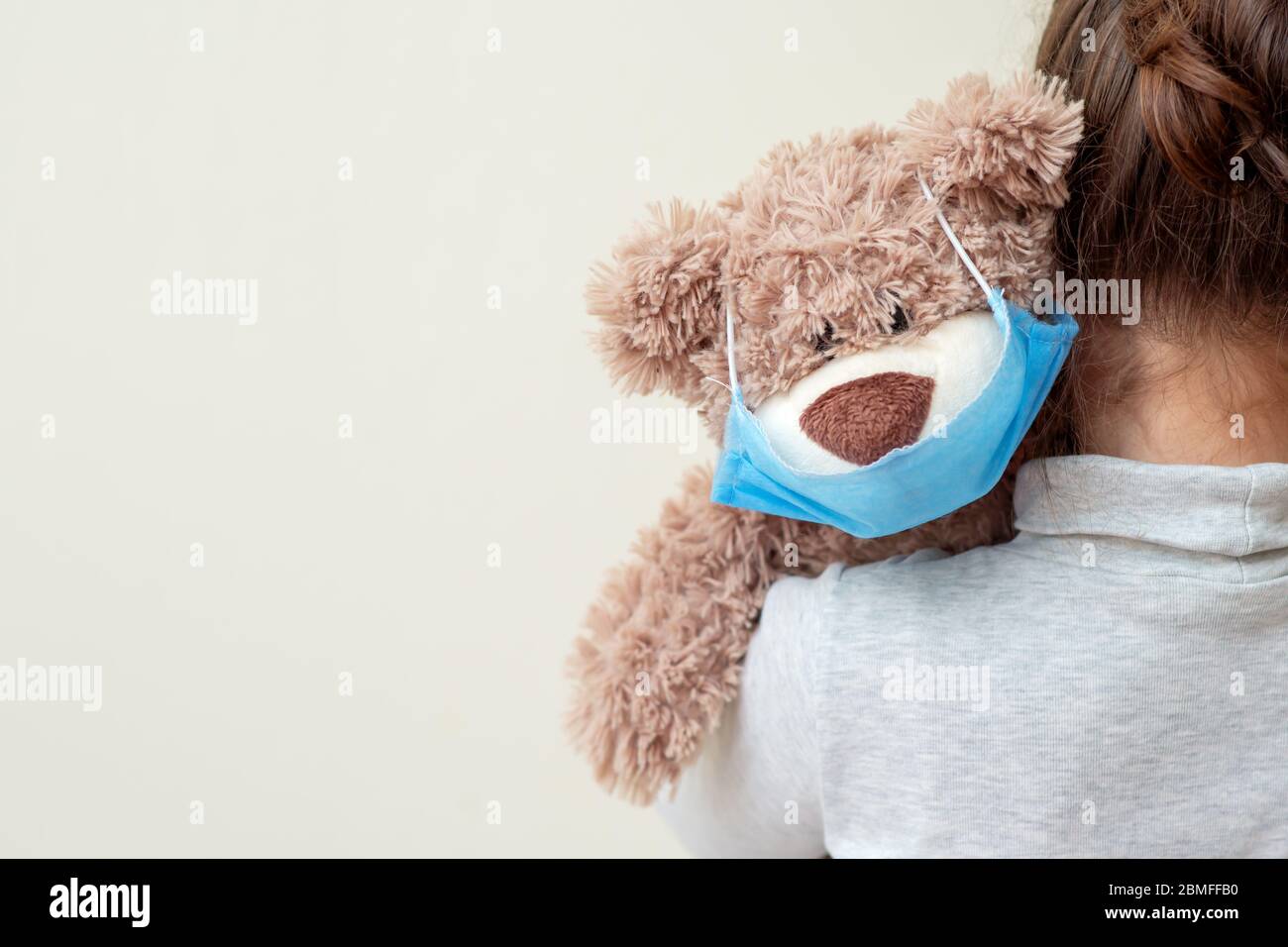 Soft toy bear with protective medical mask on child shoulder. Health care and virus protection concept. Stock Photo