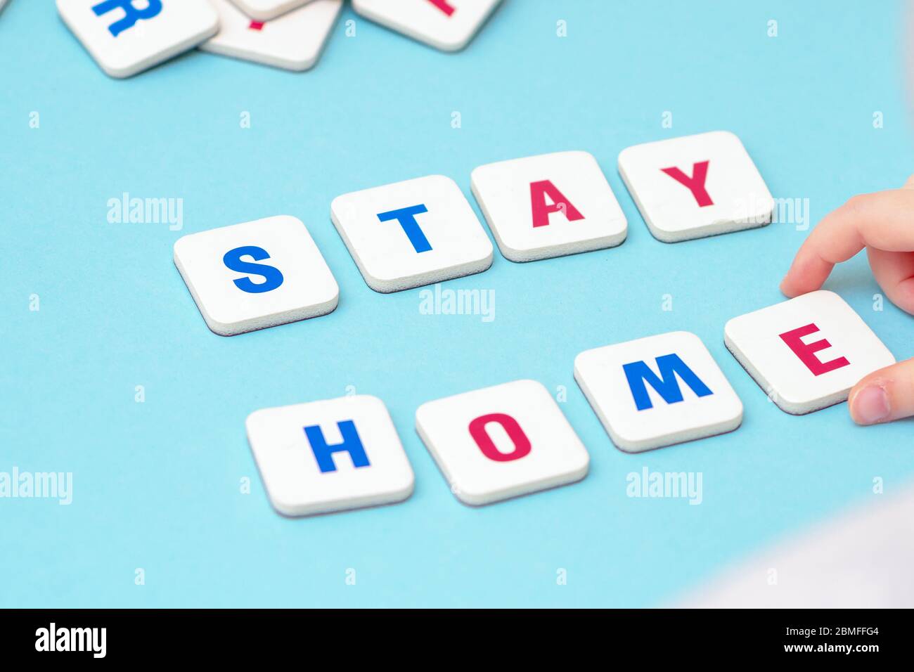 Hand of child making with letters word Stay Home on blue background. Children's creativity in quarantine. Stock Photo