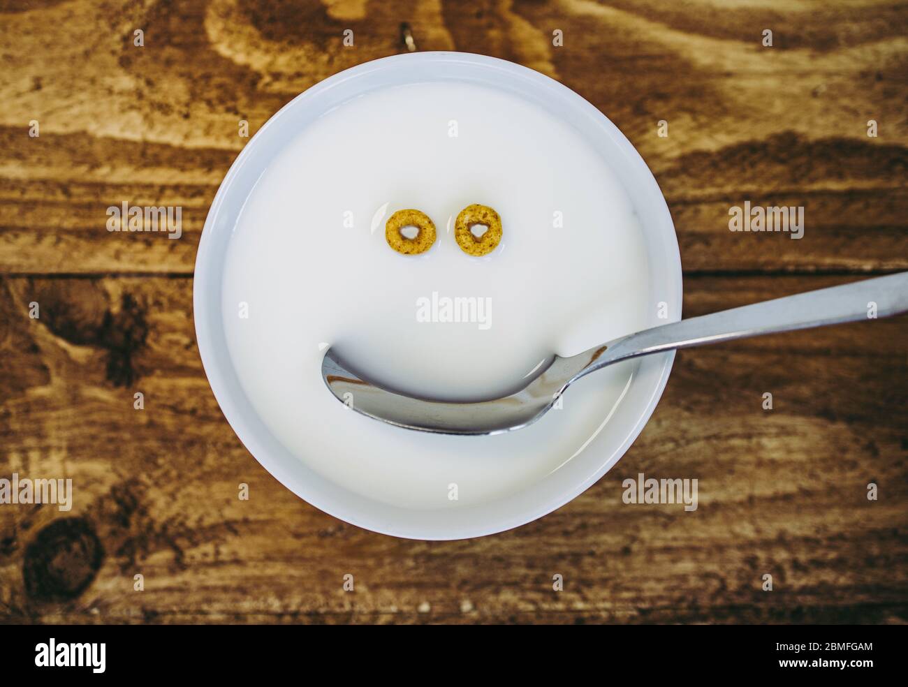 A bowl with just two pieces of round cereal left and a spoon a creating the appearance of a face in the milk Stock Photo