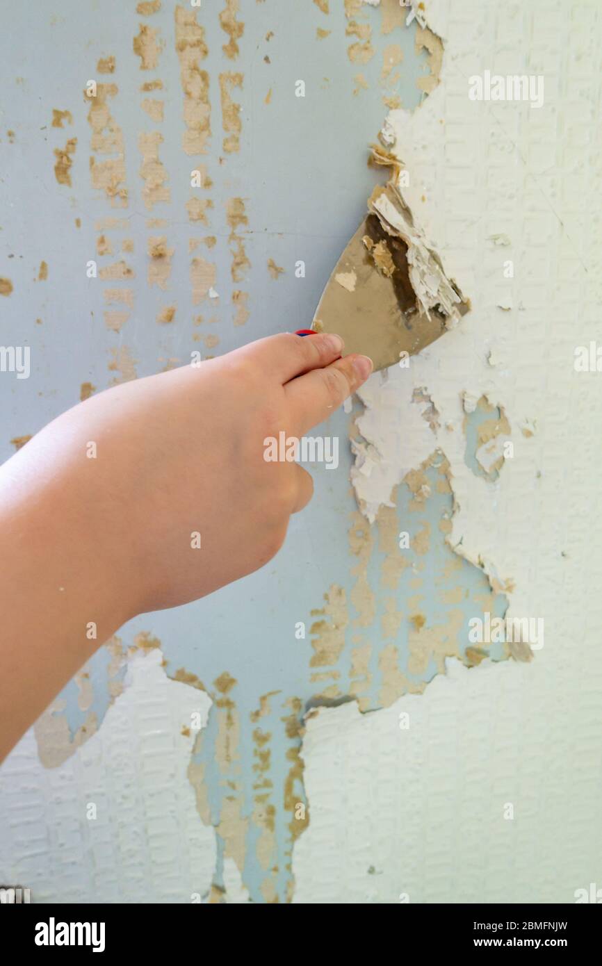 Close up of a scraper being used to strip old wallpaper from the wall