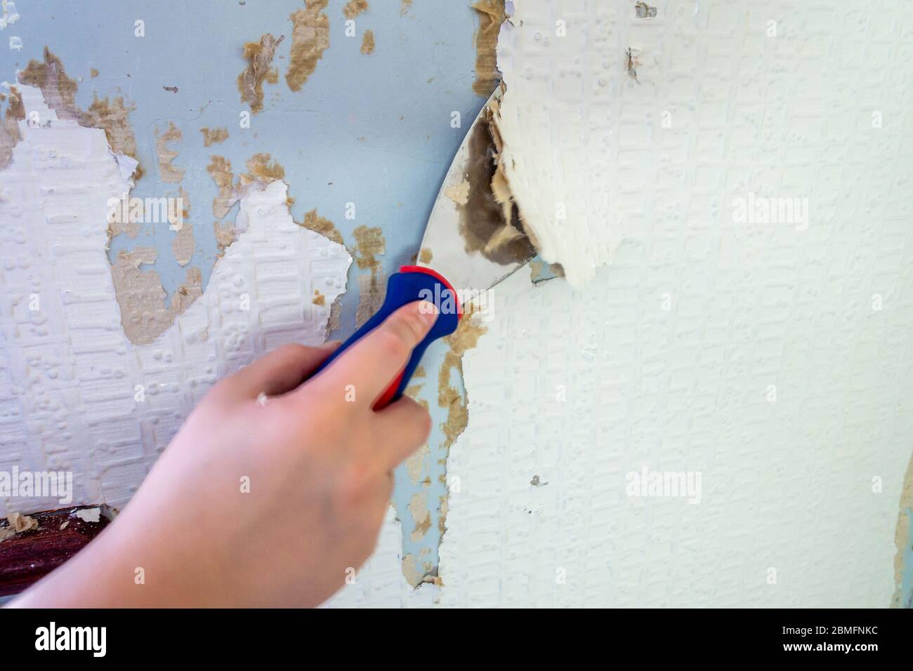 Close up of a scraper being used to strip old wallpaper from the wall