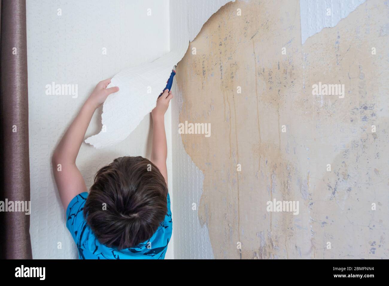 A child helps strip old wallpaper off a wall as the first stage of