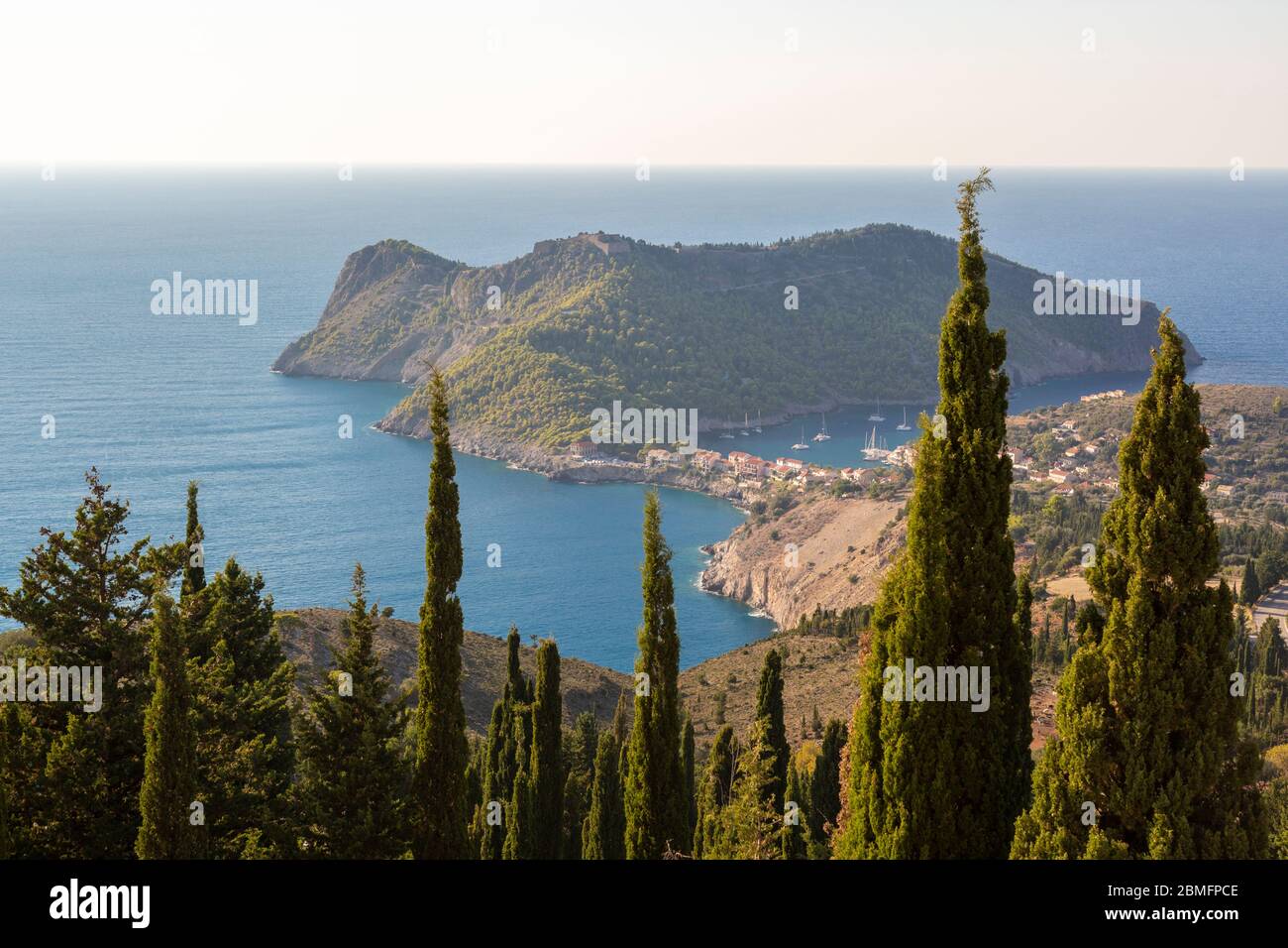 Long-range view through trees towards the traditional village of Assos, Kefalonia, Ionian Islands, Greece Stock Photo
