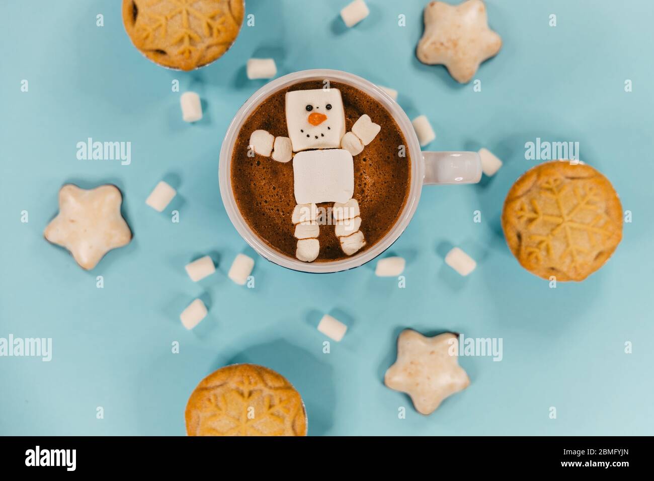 A marshmallow snowman in hot chocolate, surrounded by biscuits and mince pies Stock Photo