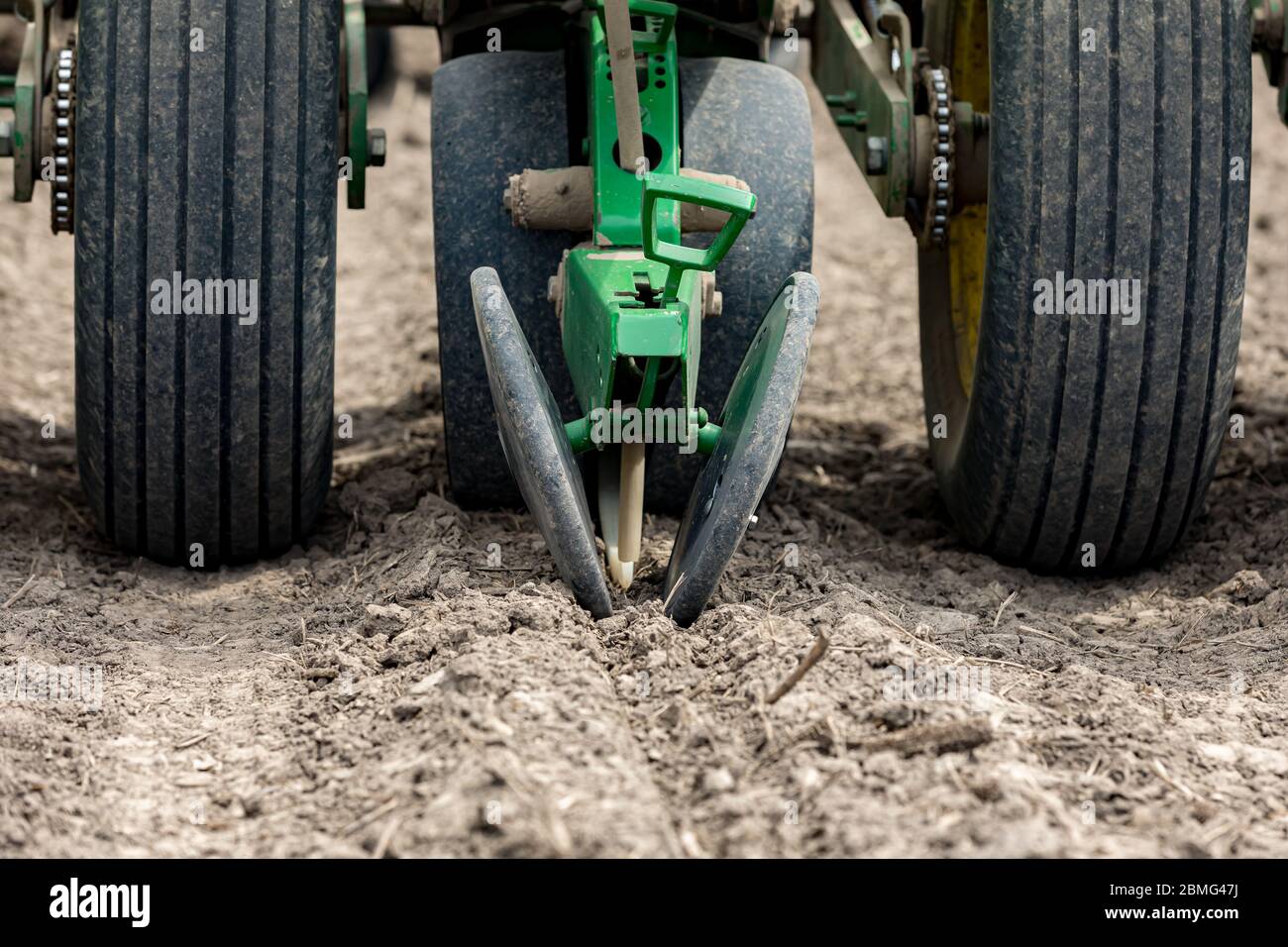 Closeup of planter in farm field planting corn or soybean seed in dry, dusty soil during spring season Stock Photo