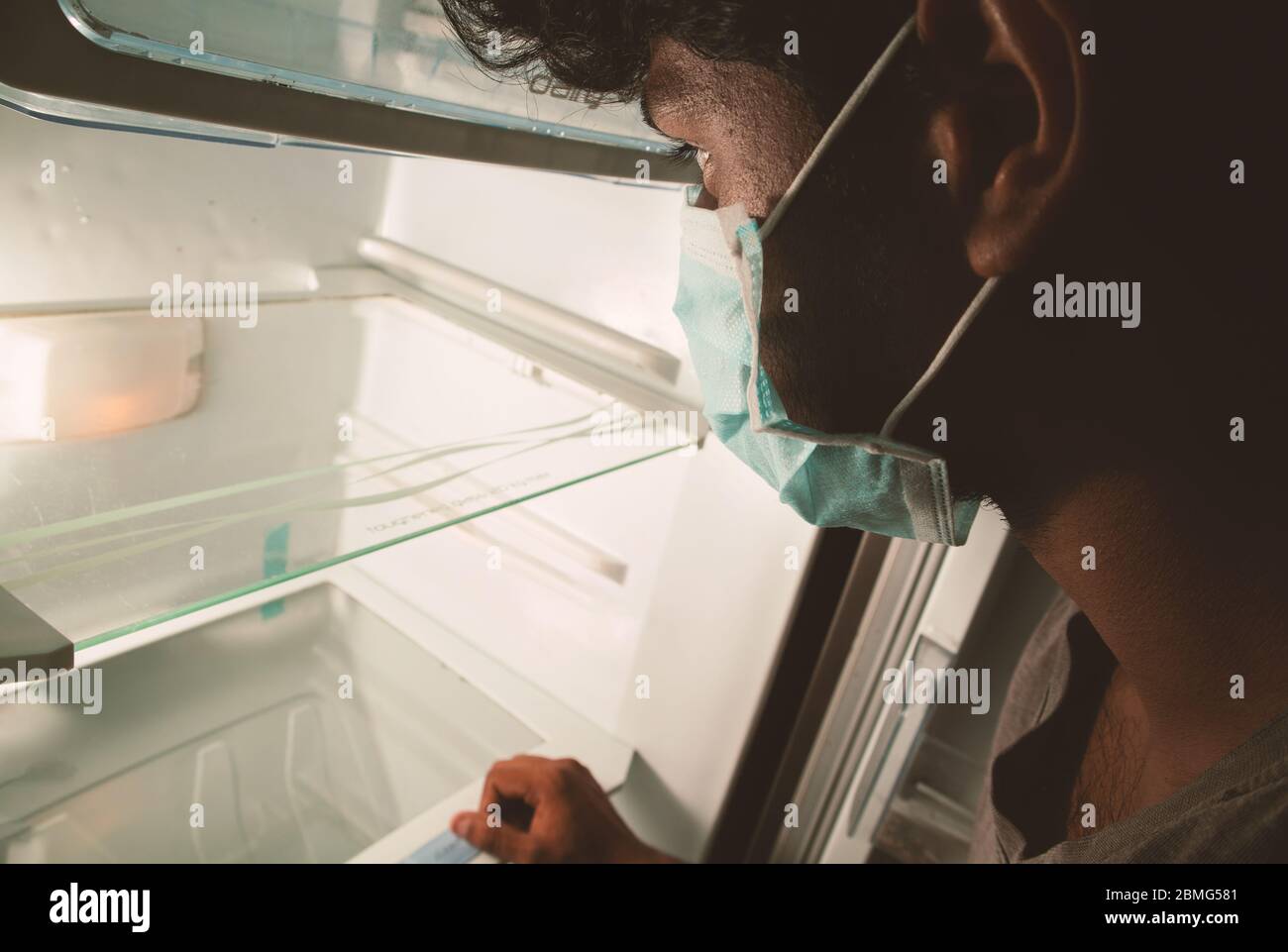 Concept of nofood available during home quarantine at covid-19 or coronavirus pandemic - Man in medical mask looking into empty fridge or refrigerator Stock Photo