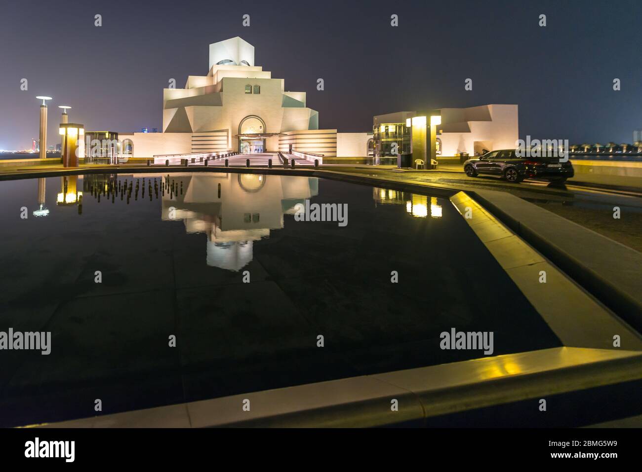 Visit of Qatar Museum of Islamic Art  in Doha mirroring in water of pond at night. Futuristic architecture near the bay of Doha. Stock Photo