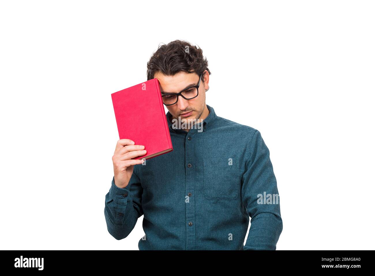 Pessimistic student guy looking down upset, as holds a book isolated on white background. Confused young man has learning troubles, negative face expr Stock Photo