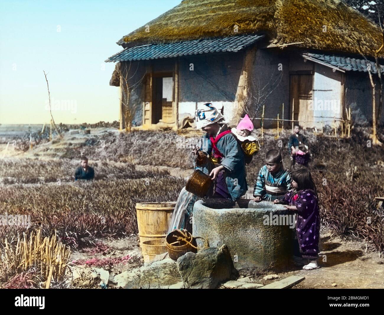 [ 1900s Japan - Japanese Mother Getting Water from Well ] —   A farmer's wife, surrounded by children, is pouring well water from a an oke (wooden bucket).  20th century vintage glass slide. Stock Photo