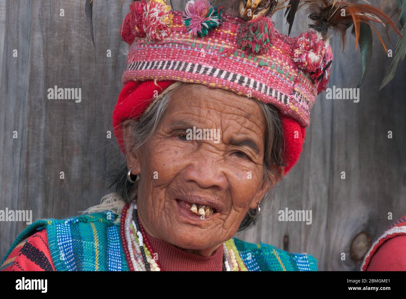 Banaue, Philippines - February 2012: Elder woman in traditional clothes sitting in front of a wooden wall Stock Photo
