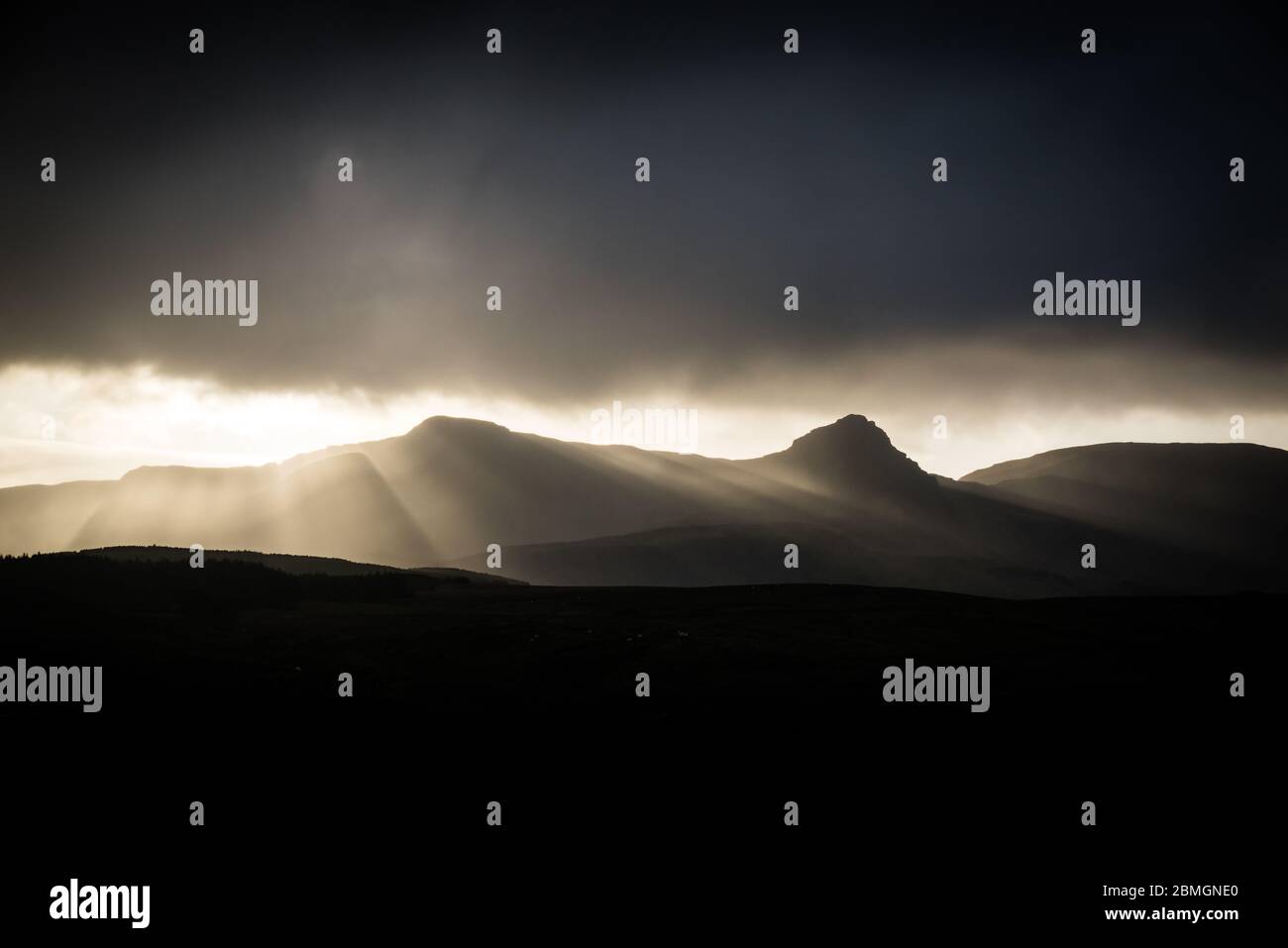 The sun sets behind the hills, blazing through a break in the clouds. Stock Photo