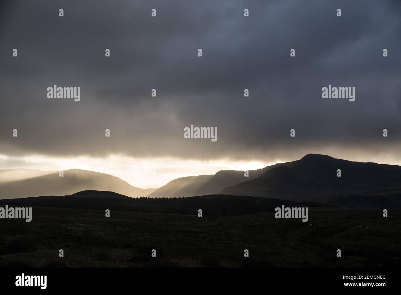 The sun sets behind the hills, blazing through a break in the clouds. Stock Photo