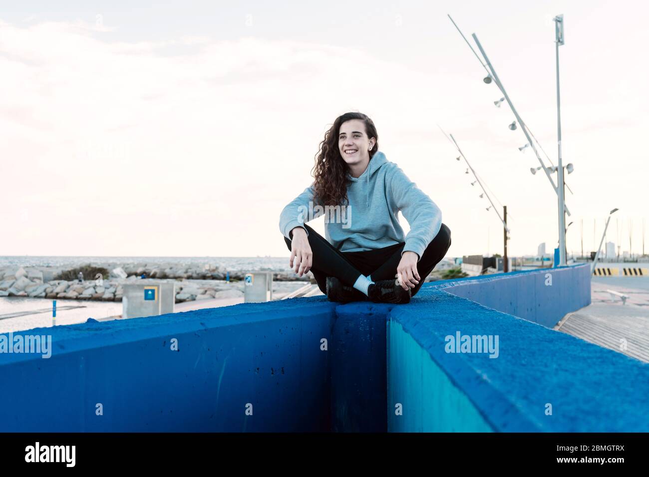 Young teenager sitting on a stone wall with her legs crossed while smiling Stock Photo