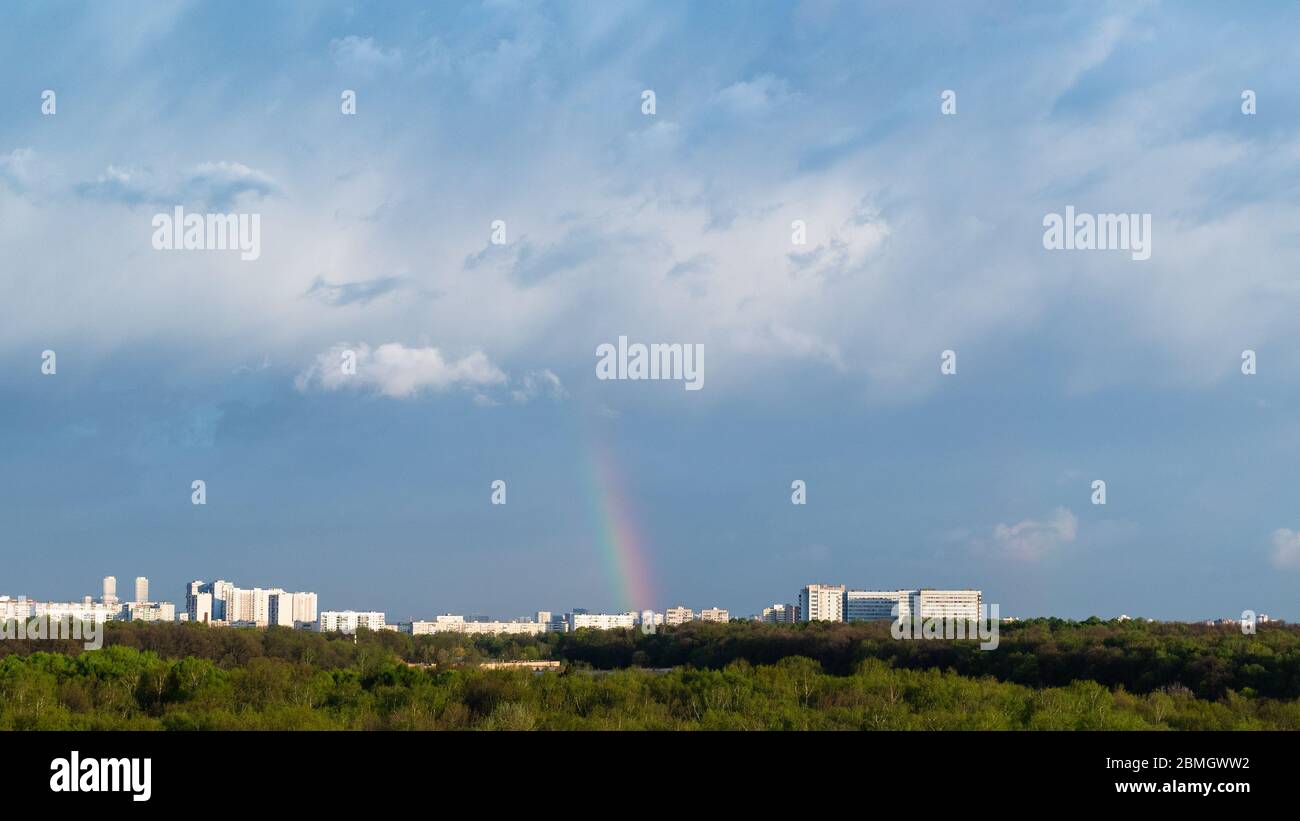 blue thunderclouds and rainbow over city on sunny spring day Stock Photo