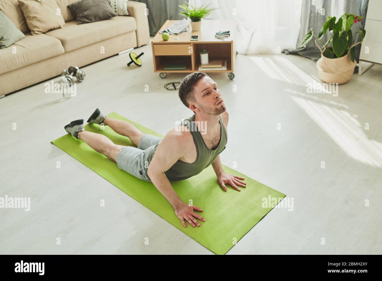 Active athlete in sportswear bending backwards while lying on mat on the floor of living-room and training in home environment Stock Photo
