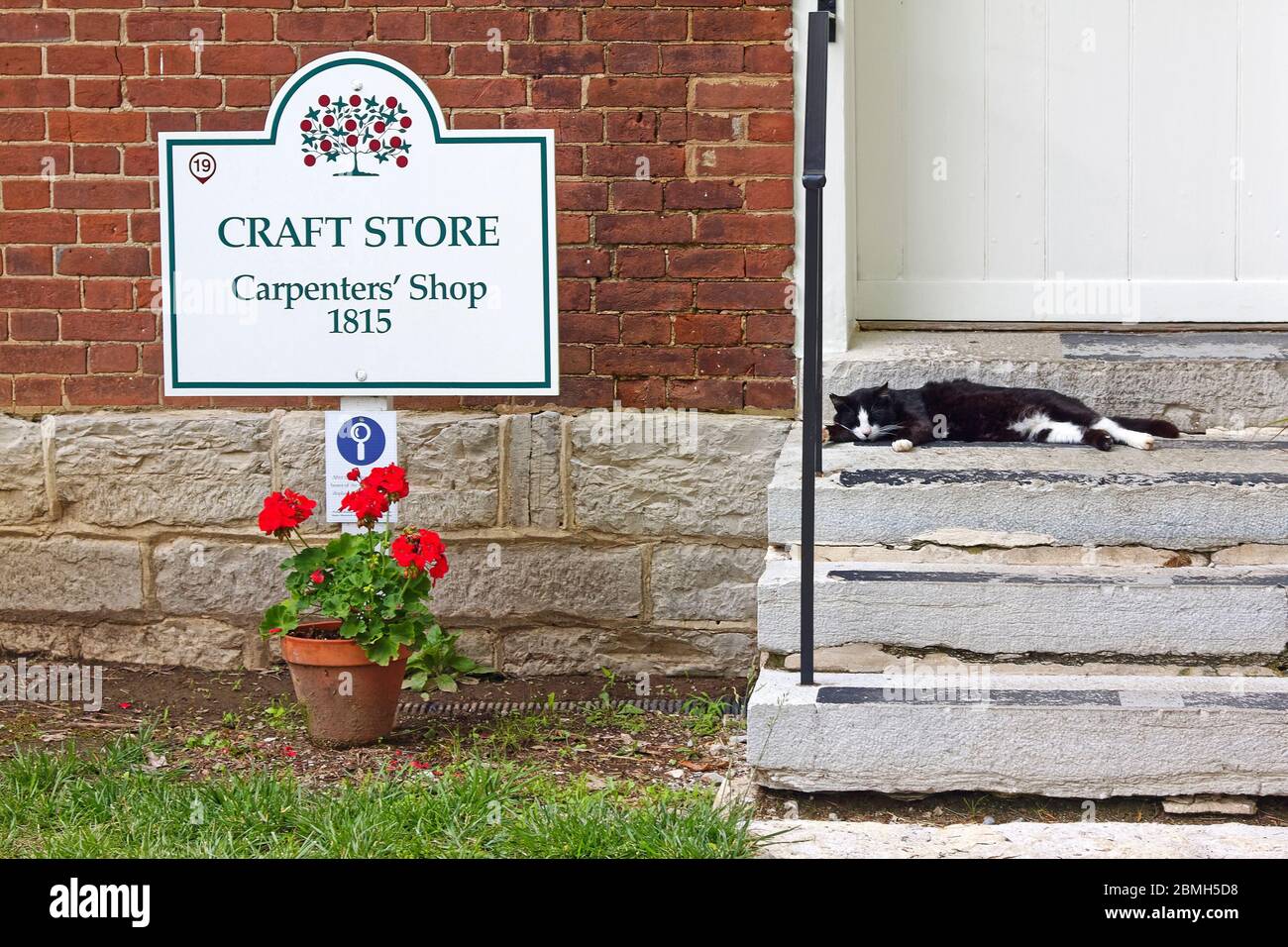 Craft Store, Carpenters' Shop building; 1815, black cat on step, potted red geranium, brick, stone, old; Shaker Village of Pleasant Hill; defunct reli Stock Photo