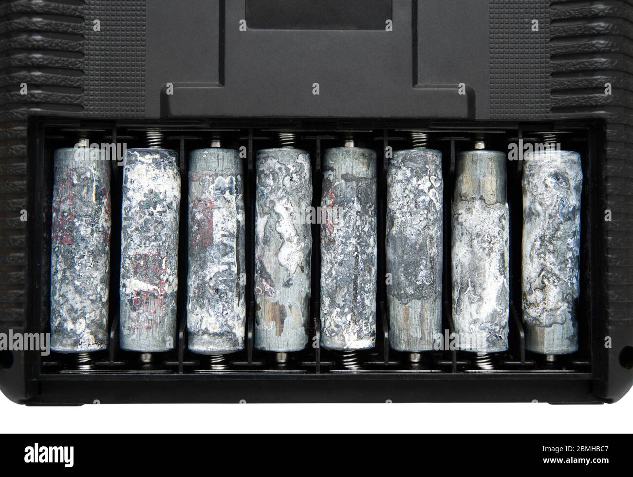 A row of eight unwrapped and heavily oxidized AA batteries inside the battery compartment of an electronic device. Stock Photo