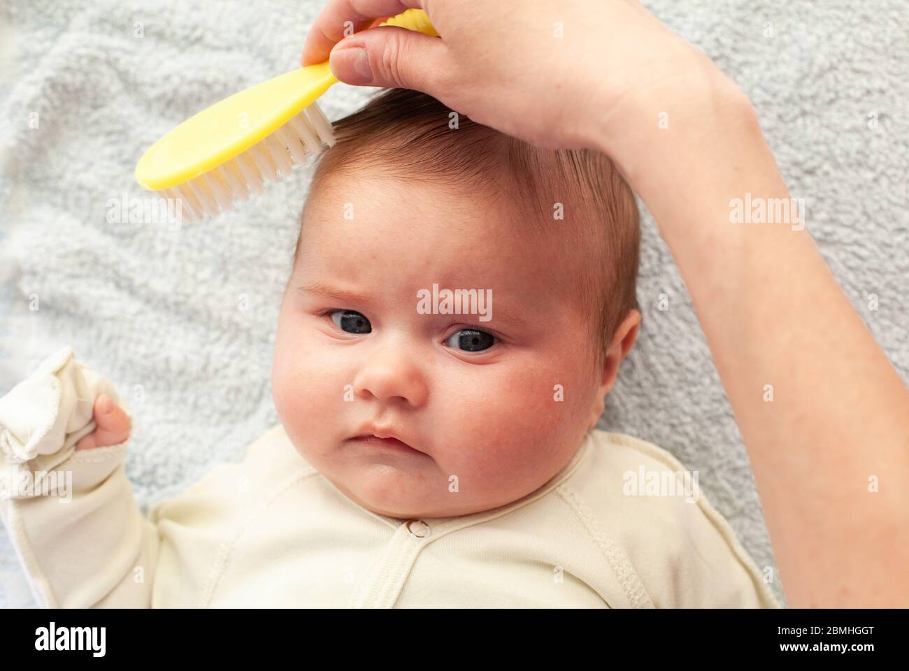 Mom combs a newborn baby with a special hair brush. Baby hygiene Stock