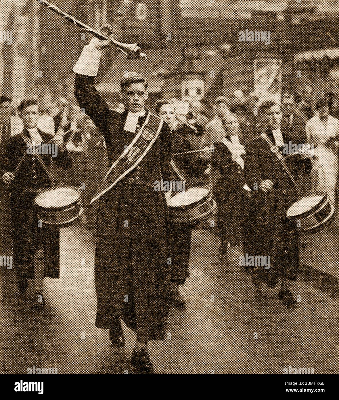 An historic press photograph of the band of Christ's Hospital (Blue Coat School) near Horsham, UK marching in their traditional costumes.The boys uniforms have not altered in design since Tudor times  and  consists of a long blue (symbol of charity) belted coat,  matching knee breeches, yellow socks and white neck bands. Girls are also admitted and wear similar uniforms but with a plaited skirt. Uniforms are provided free, a tradition from the earliest times when the school educated  ‘fatherless and poor children’ and the uniforms were provided from donations. The school is now fee paying. Stock Photo